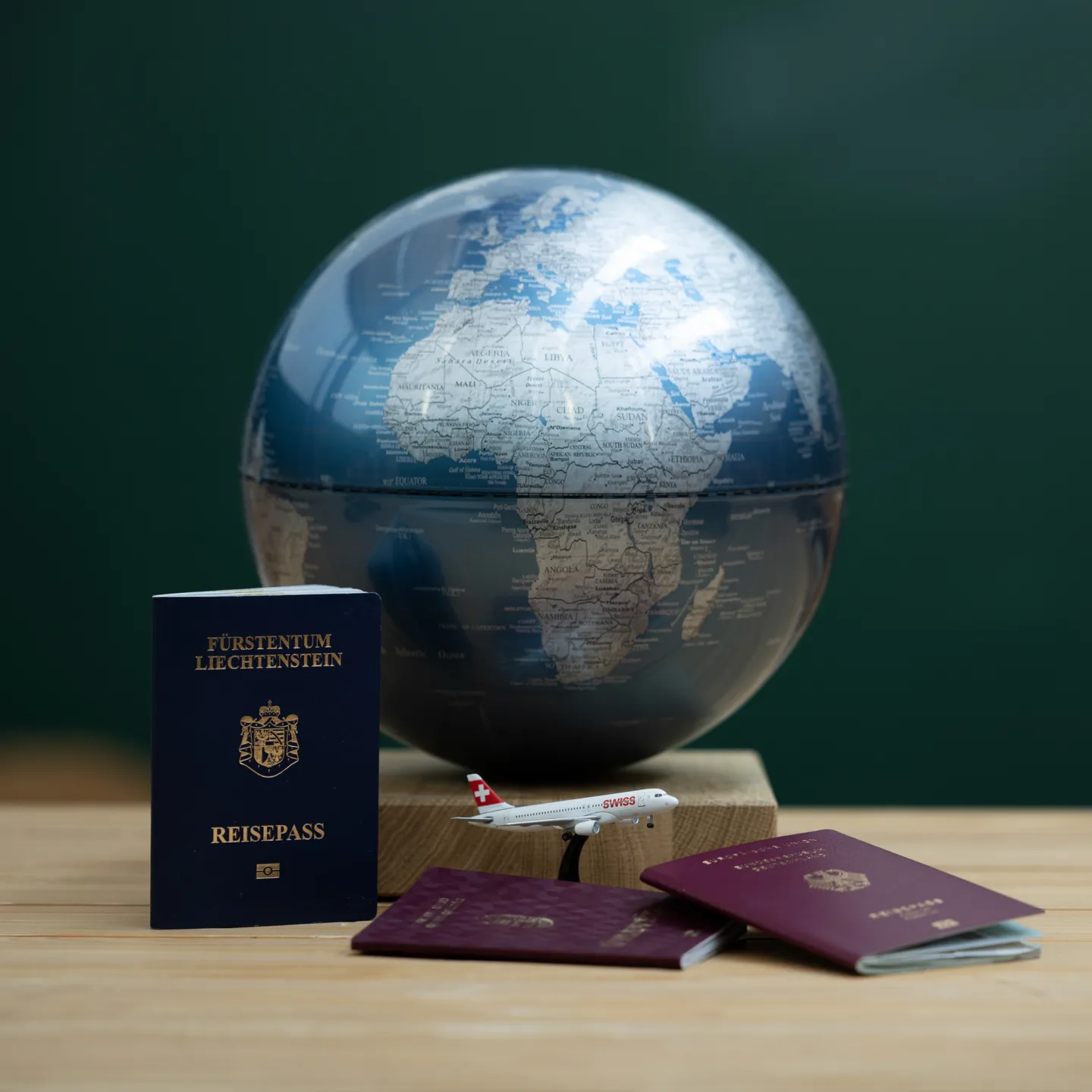 Globus mit Reisepässen aus Liechtenstein und EU sowie Modellflugzeug auf Tisch.