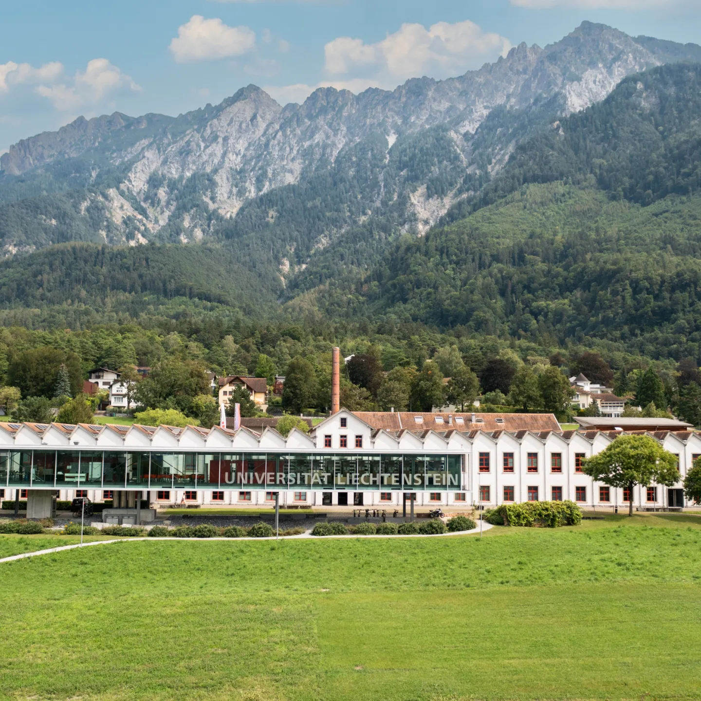 Frontansicht der Universität Liechtenstein mit markanter Glasfassade und grüner Wiese im Vordergrund.