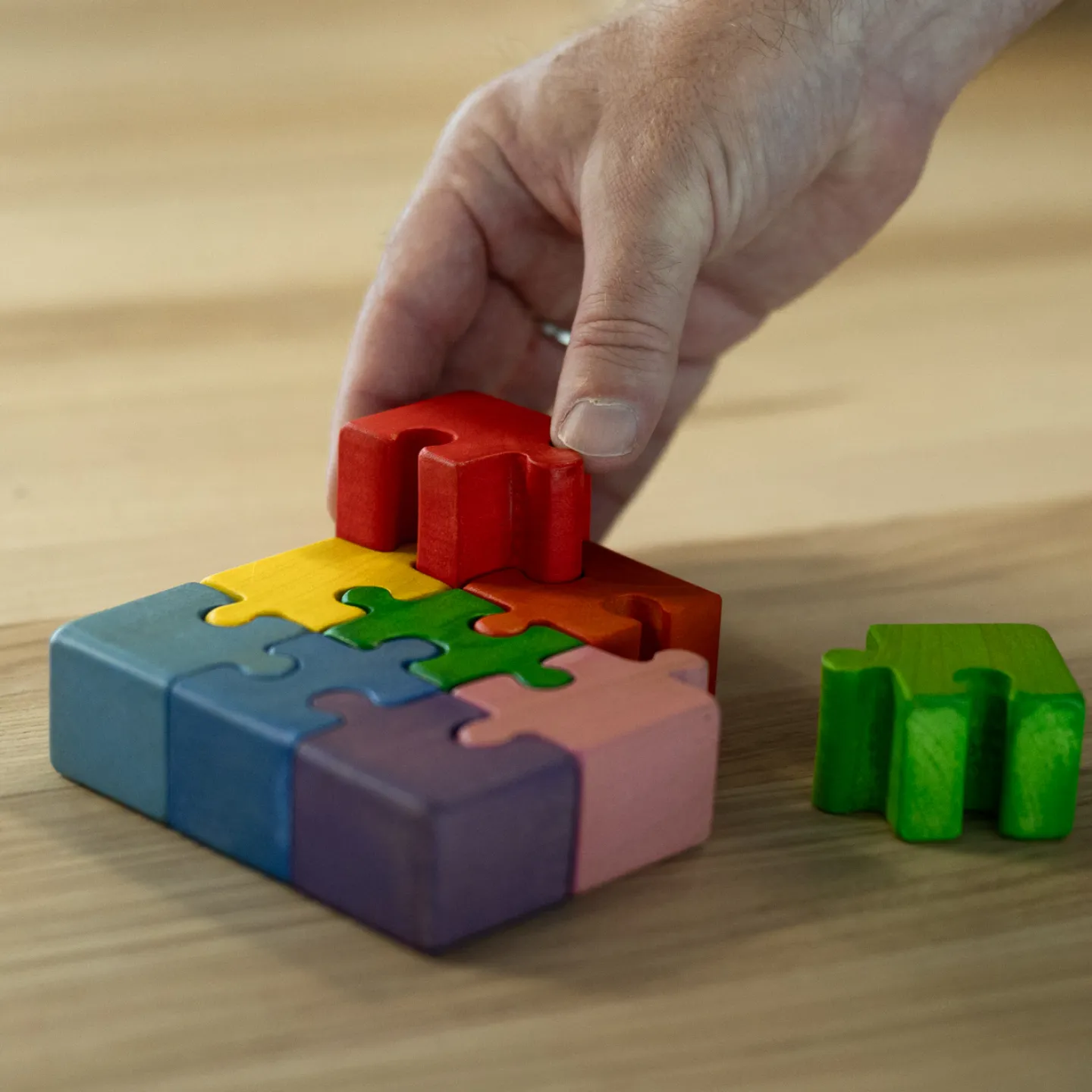 Hand setzt buntes Holzpuzzle auf Holztisch in der Universität Liechtenstein zusammen.