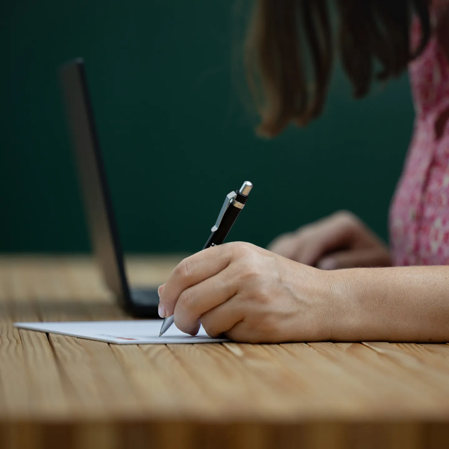 Person schreibt mit Stift auf Papier vor Laptop im Arbeitsraum der Universität Liechtenstein.