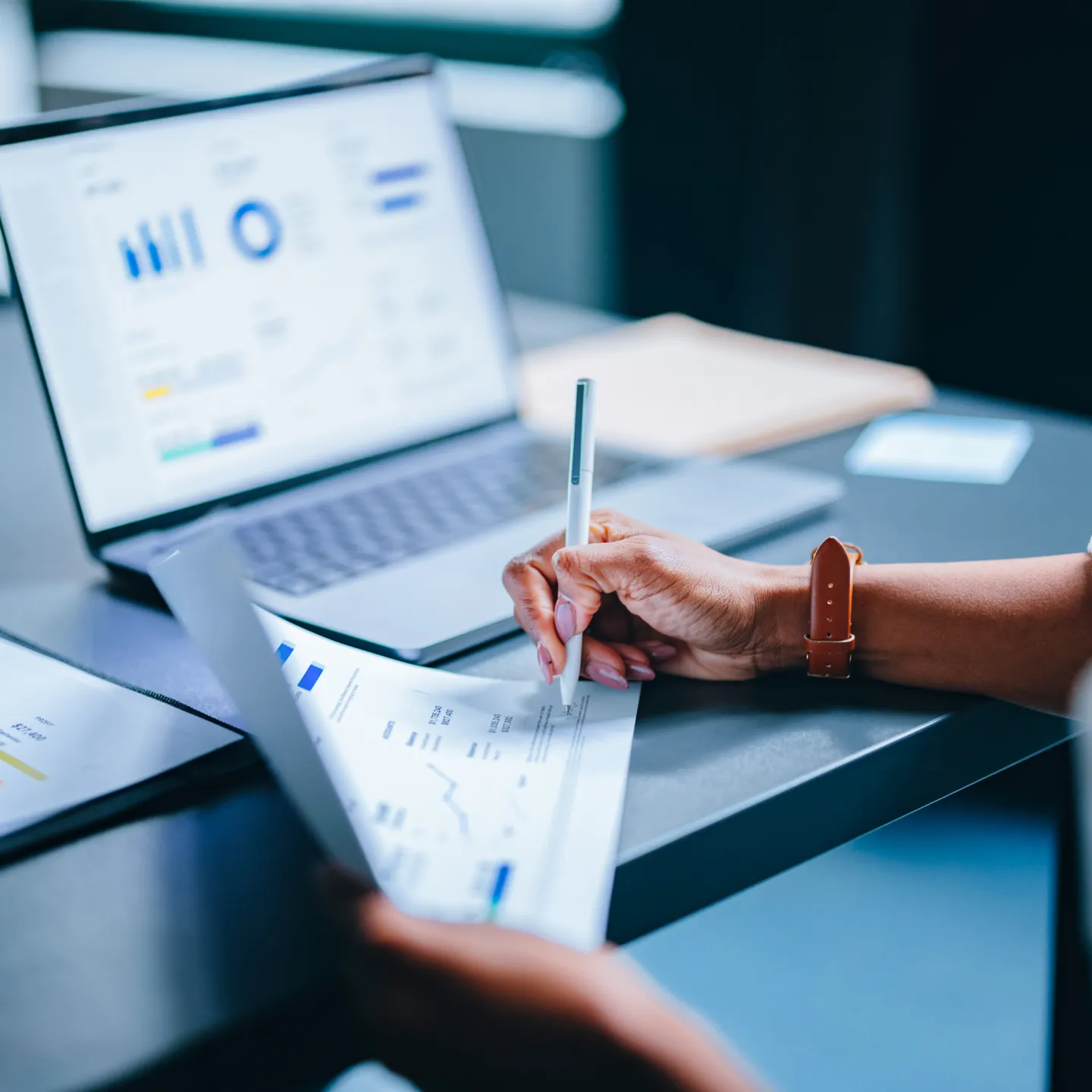 Hand schreibt Notizen zu Finanzstatistiken vor geöffnetem Laptop mit Diagrammen und Tabellen.