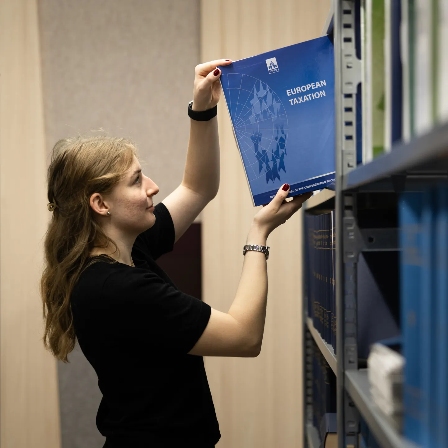 Frau holt Zeitschrift European Taxation aus Regal in der Bibliothek der Universität Liechtenstein.