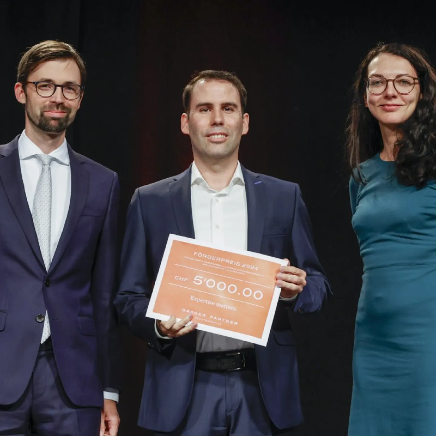 PD Dr. Bernhard Burtscher, Alois Wille und Dr. Christina Preiner mit einem Preis auf dem 5000 CHF steht.