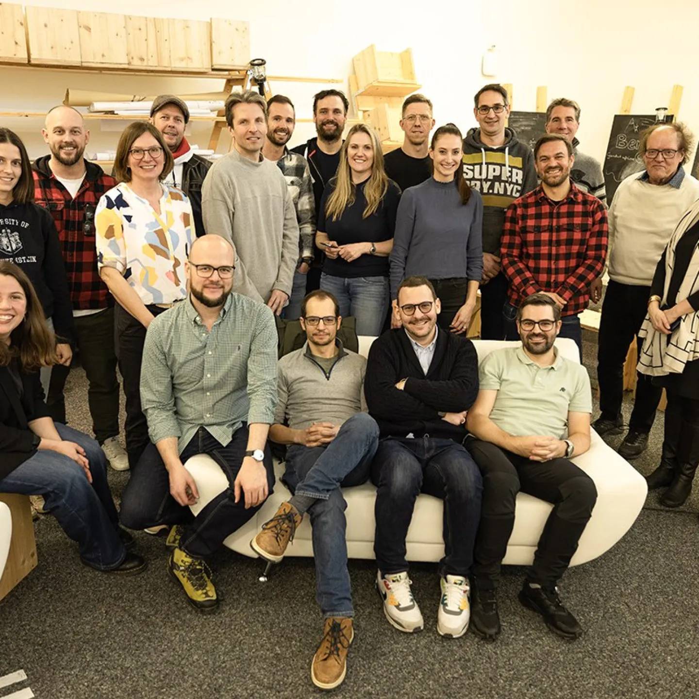 Gruppenfoto von Absolventen des Masterprogramms in Entrepreneurship der Universität Liechtenstein, die sich in einem Raum mit Regalen und Tafeln versammelt haben. Die Personen lächeln und stehen oder sitzen in zwei Reihen.