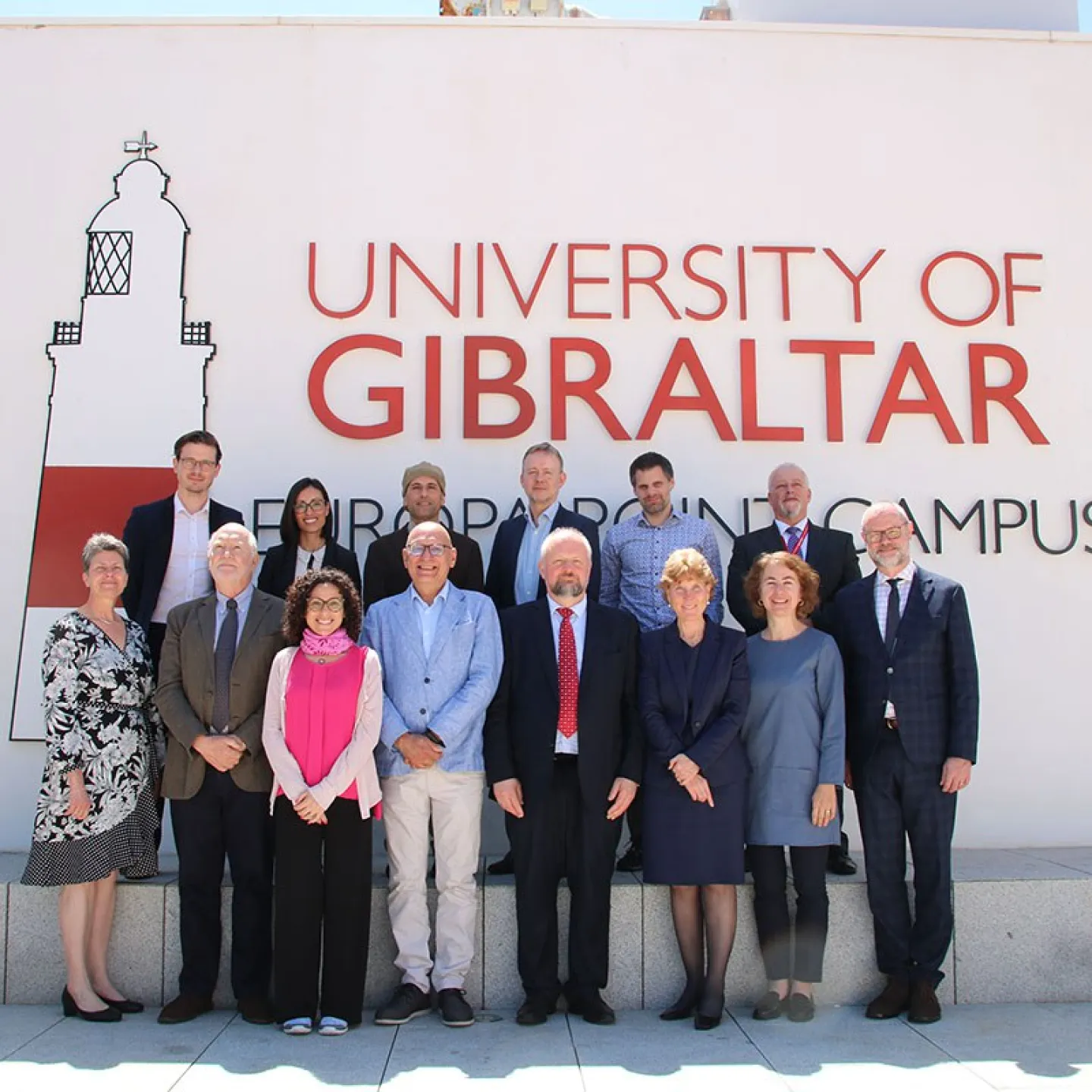 Eine Gruppe von Personen steht vor einem Gebäude mit der Aufschrift "University of Gibraltar". Sie posieren für ein Gruppenfoto bei sonnigem Wetter.