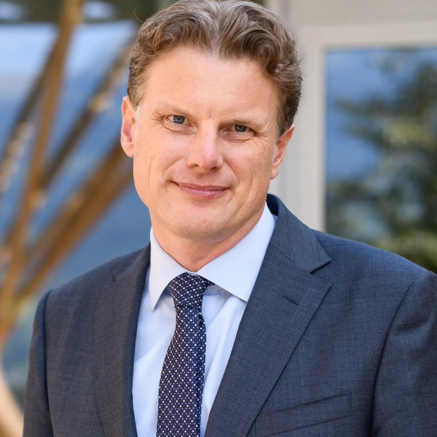 Ein Mann in einem Anzug steht lächelnd vor einem Gebäude.