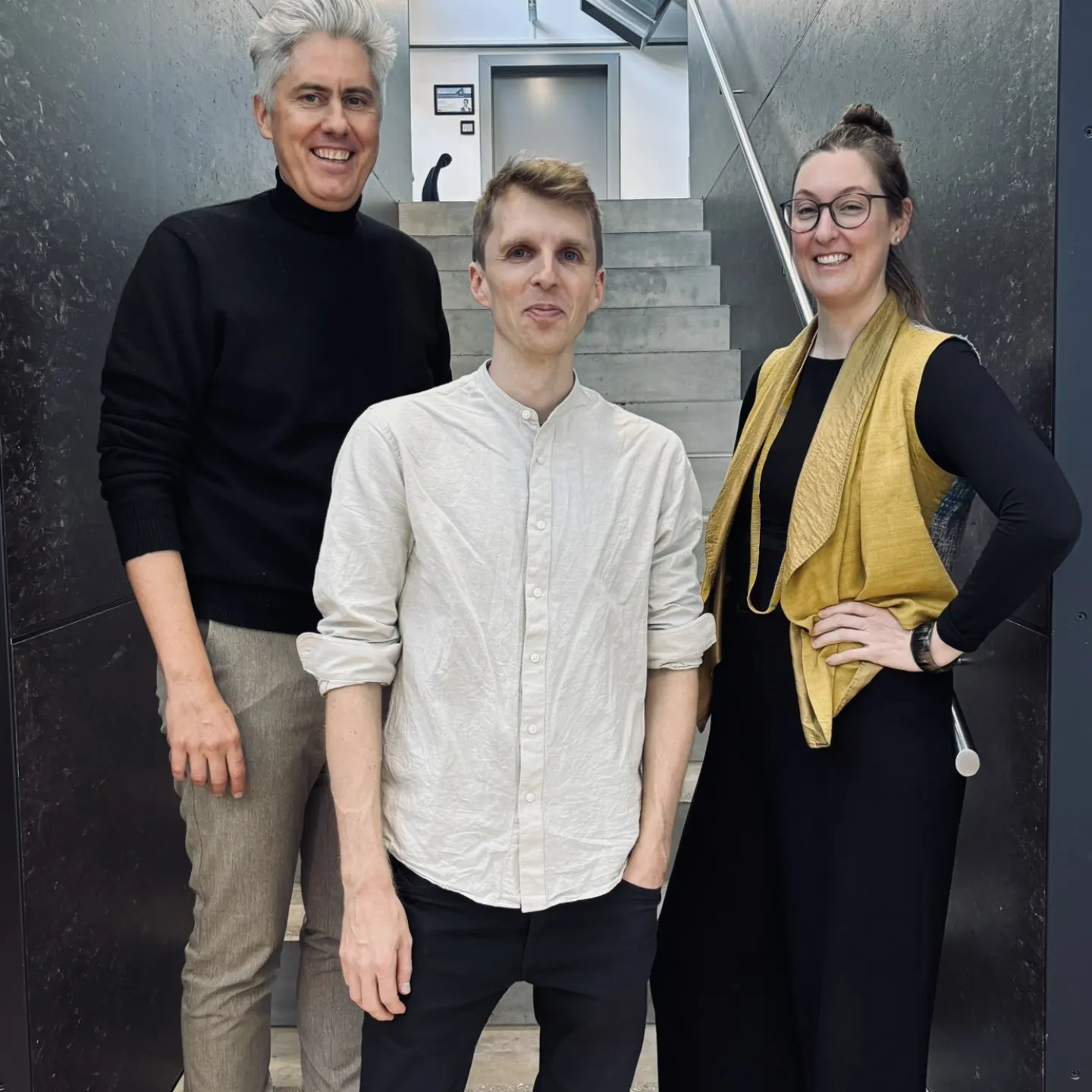 Drei Personen auf einer grau/schwarzen Treppe