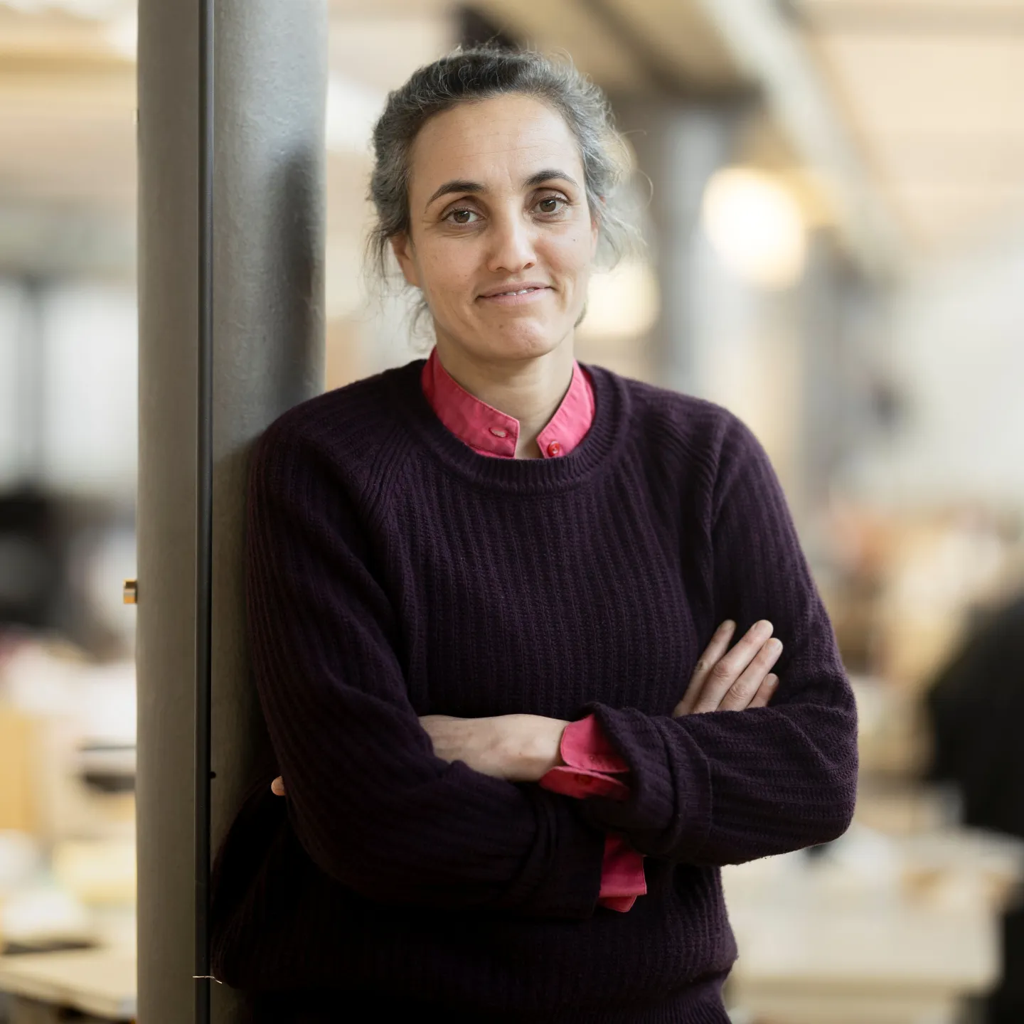 Porträt einer Frau mit schwarzem Pullover, die mit verschränkten Armen an einer Säule lehnt