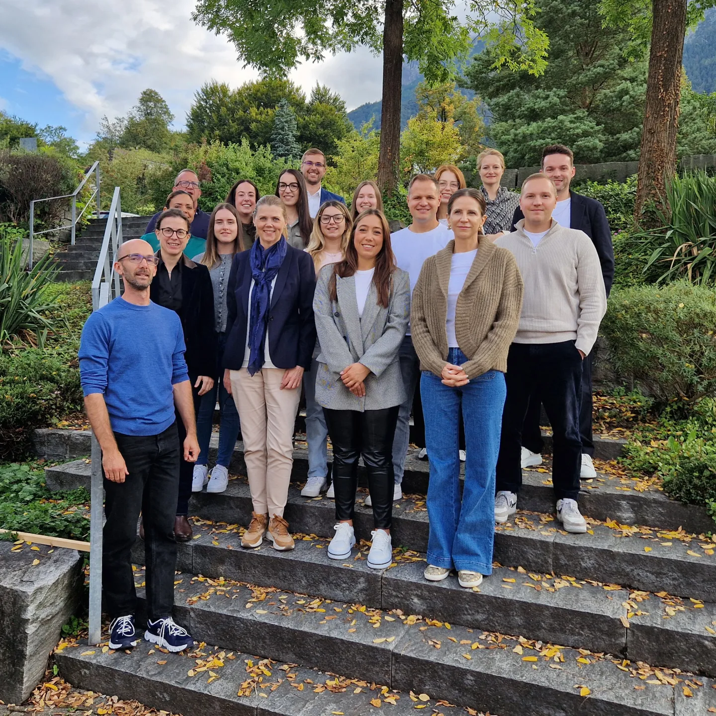 Gruppe von Erwachsenen steht auf Treppe in grüner Umgebung.