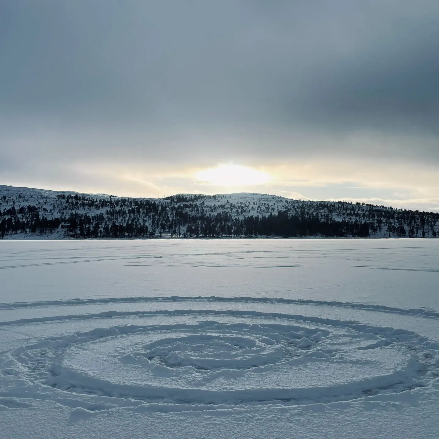 Spiralförmige Spur im Schnee auf gefrorenem See vor Hügeln.