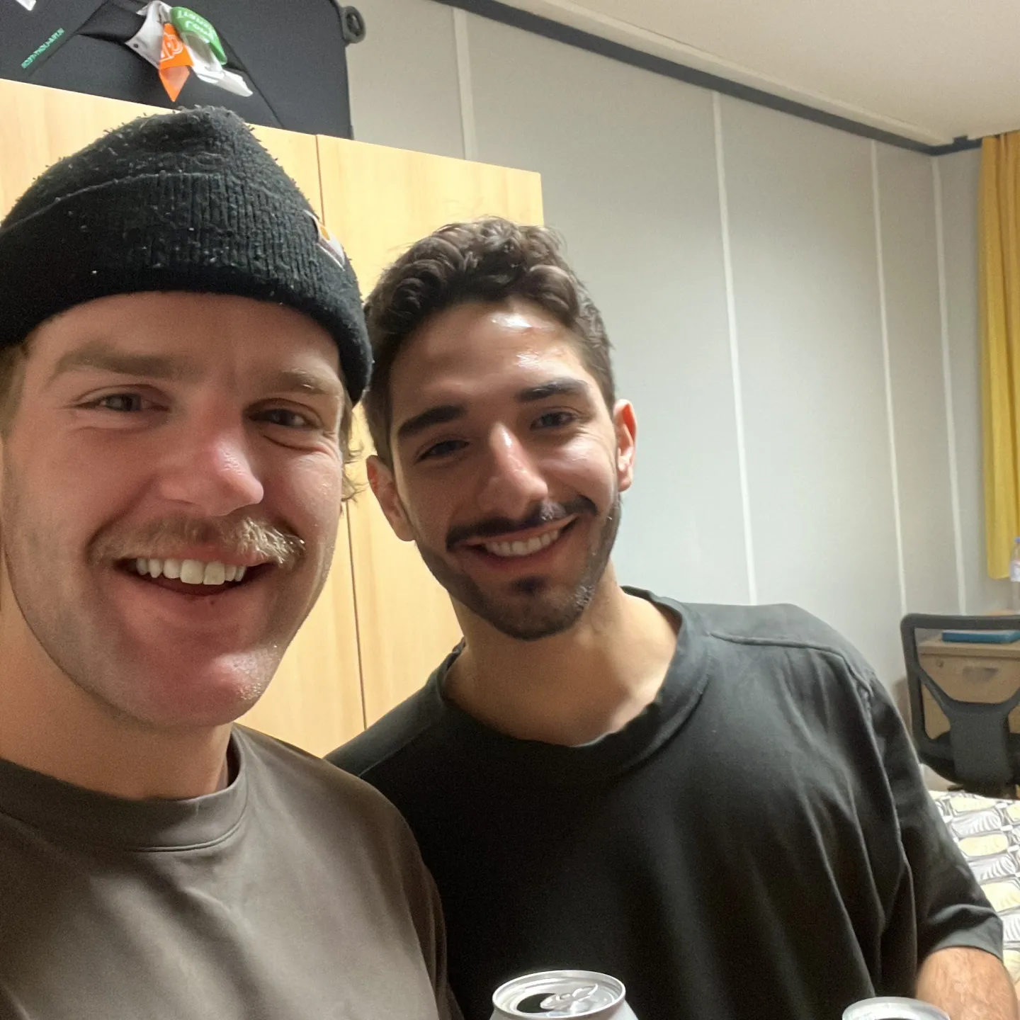 Zwei Studierende halten lächelnd Getränkedosen in die Kamera.