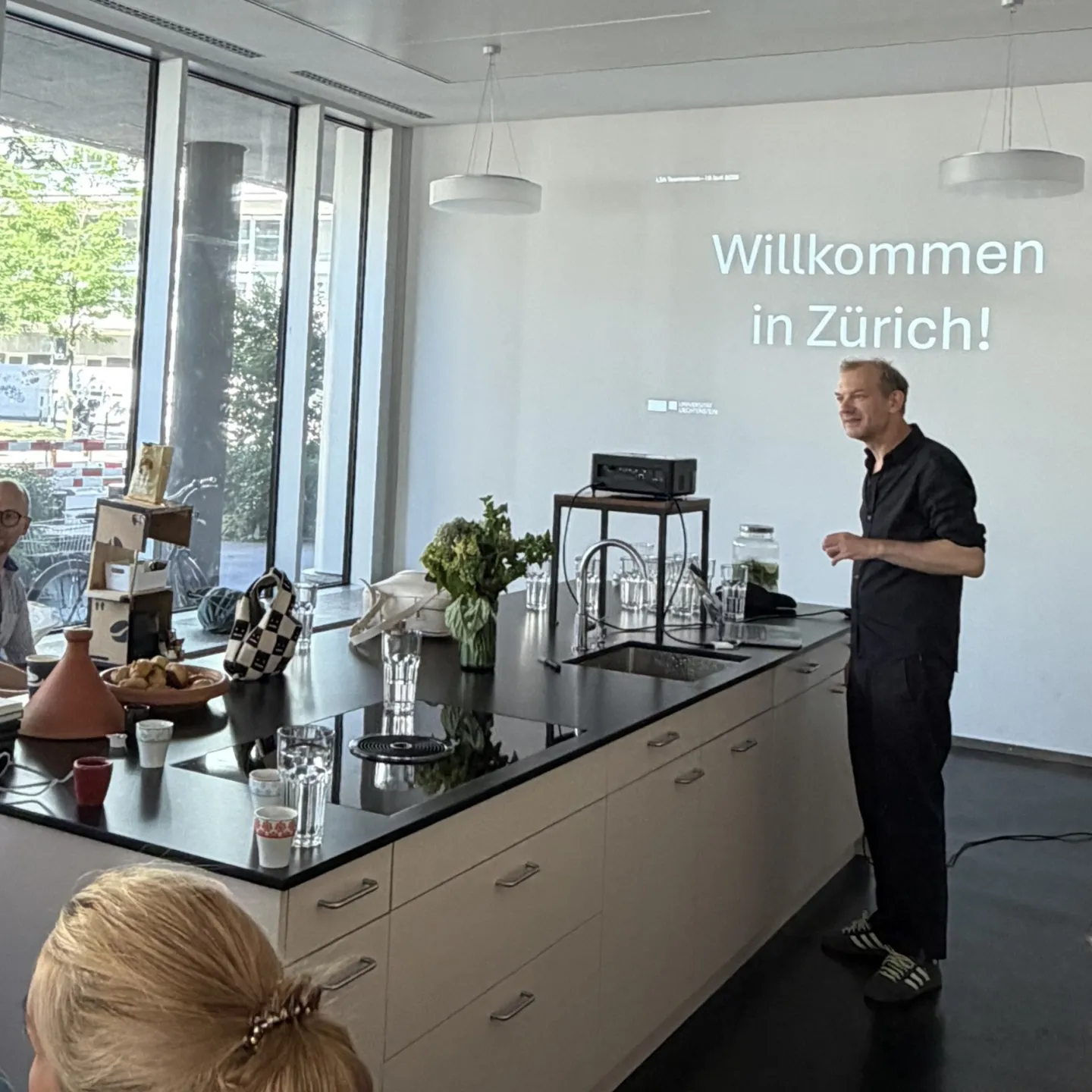 Vortragender an einem weissen Küchenblock mit Projektion an der Wand 