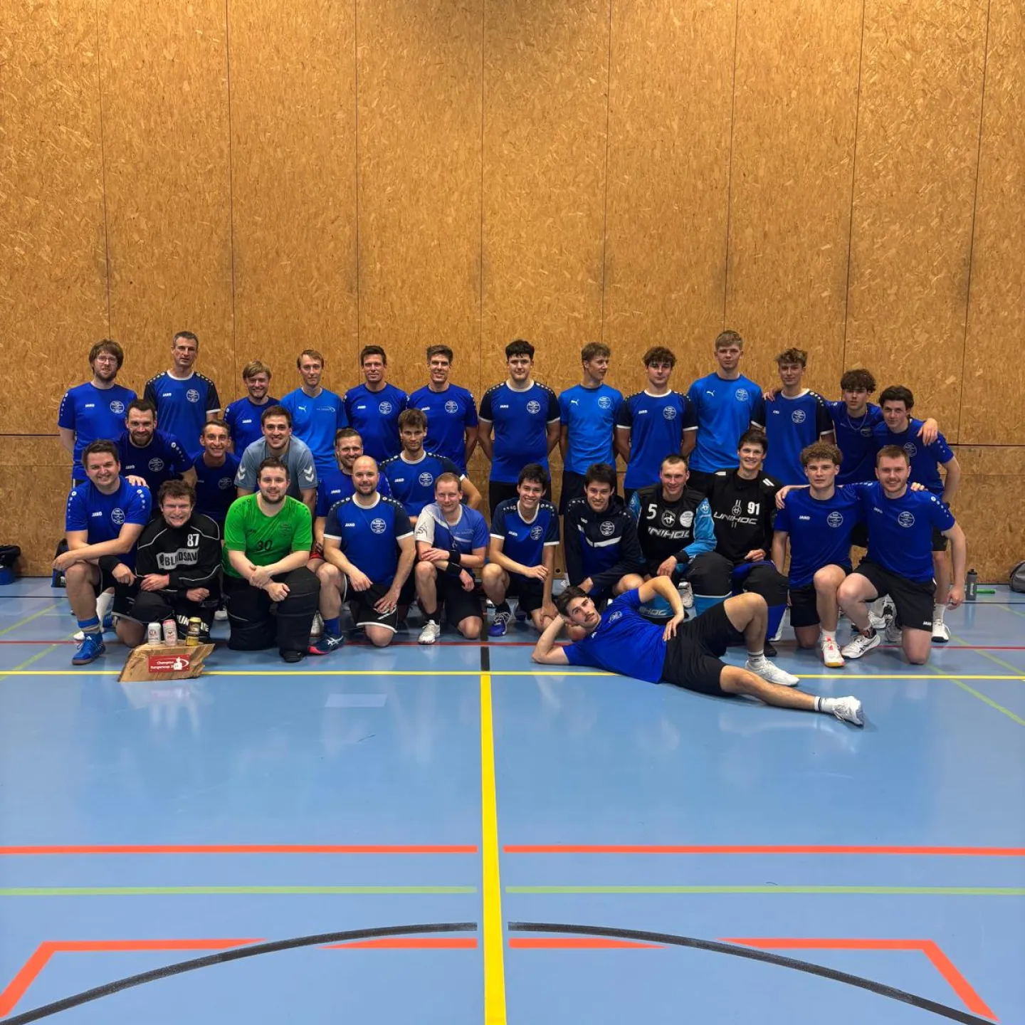 Group photo of a handball team wearing blue jerseys in a sports hall.