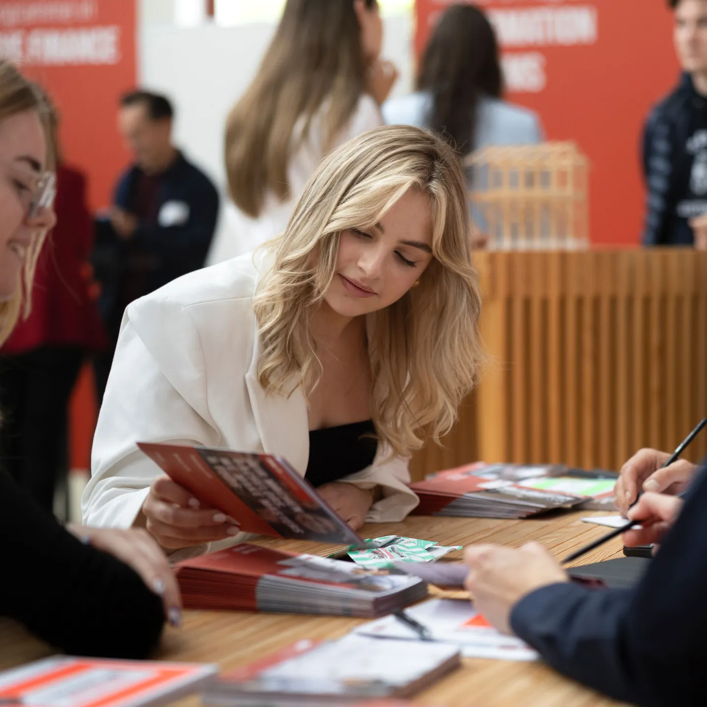 Eine Mitarbeiterin der Universität Liechtenstein berät einen Studieninteressierten an einem Informationsstand und zeigt ihm Informationsmaterialien.