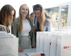 Drei neue Studentinnen stehen am Campus der Universität Liechtenstein am Welcome Day vor einem Stapel von Taschen
