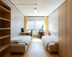 Helles Doppelzimmer mit zwei Betten, Schreibtischen und großem Fenster im Studierendenwohnheim der Universität Liechtenstein.