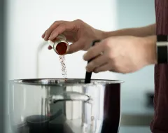 Student würzt ein Gericht mit rotem Gewürz in einem Kochtopf in der modernen Gemeinschaftsküche des Studierendenwohnheims.