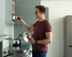 Student räumt Kochgeschirr in einen Oberschrank der Gemeinschaftsküche im Studierendenwohnheim der Universität Liechtenstein.