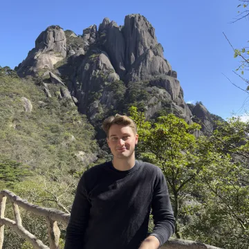 Studierender der Universität Liechtenstein vor markanter Felsformation in einer Berglandschaft während Auslandsaufenthalt