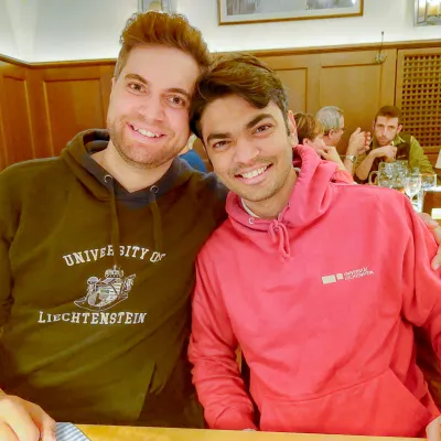 Zwei Alumni der Universität Liechtenstein lächeln in einem gemütlichen Restaurant in die Kamera.