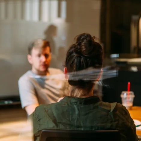 Frau sitzt Rücken gewandt zur Kamera im Meeting Raum