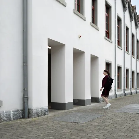 Studentin geht in ein weißes Universitätsgebäude mit roten Fenstern an der Universität Liechtenstein.