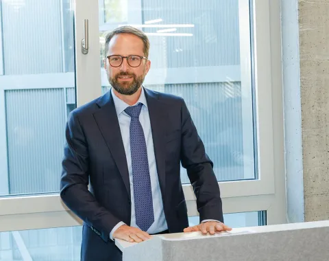 Ein Mann im Anzug steht an einem Rednerpult vor einem Fenster.