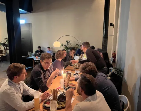 Alumni-Treffen in einem gemütlichen Restaurant: Mehrere Personen sitzen an einem langen Tisch, unterhalten sich und genießen Speisen und Getränke in entspannter Atmosphäre.