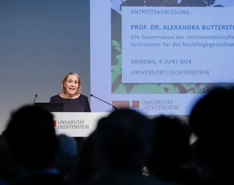 Eine Person hält eine Antrittsvorlesung im Auditorium der Universität Liechtenstein. Im Hintergrund ist eine Präsentationsfolie mit dem Titel der Vorlesung und dem Datum zu sehen. Das Publikum sitzt im Vordergrund.
