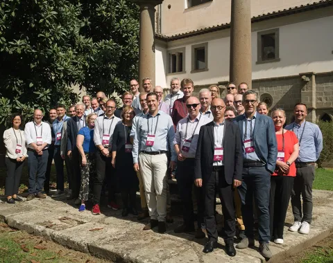 Gruppe von Menschen steht draußen vor einem historischen Gebäude während des ERCIS-Workshops in Viterbo, Italien. Sie tragen Namensschilder und lächeln in die Kamera.