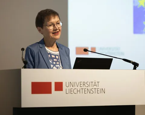 Eine Frau steht am Rednerpult im Auditorium der Universität Liechtenstein. Vor ihr steht ein Laptop, hinter ihr ist eine Präsentation zu sehen.