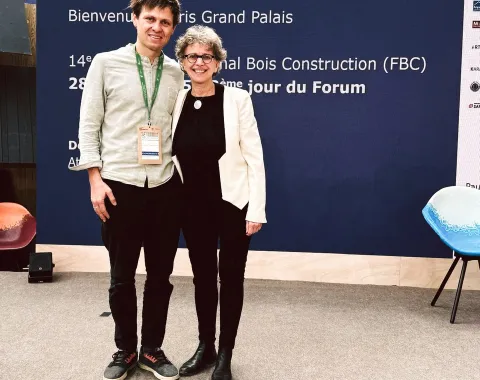 Zwei Personen stehen auf einer Bühne vor einem blauen Banner mit der Aufschrift „Forum Bois Construction“ im Grand Palais, Paris. Sie lächeln in die Kamera.