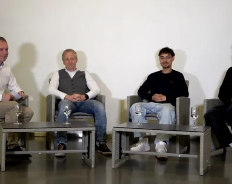 Vier Männer sitzen in einer Gesprächsrunde auf grauen Sesseln. Vor ihnen stehen zwei niedrige Tische mit Wassergläsern. Im Hintergrund sind Pflanzen zu sehen. Oben rechts befindet sich das Logo des Campus Radio der Universität Liechtenstein.