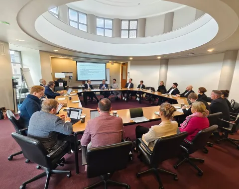 Teilnehmende einer Studienreise sitzen in einem modernen Konferenzraum an einem ovalen Tisch. Eine Präsentation wird auf einem Bildschirm gezeigt.