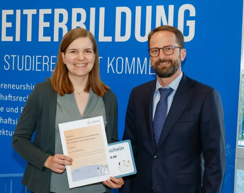 Eine Absolventin des Zertifikatsstudiengangs Treuhandwesen an der Universität Liechtenstein erhält eine Auszeichnung. Sie steht neben einem Mann vor einem blauen Hintergrund mit dem Schriftzug "Weiterbildung".