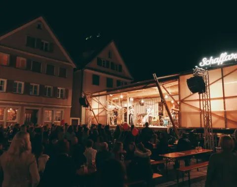 Eine beleuchtete Bühne des Base Camps der Universität Liechtenstein bei Nacht, umgeben von einem Publikum. Die Bühne ist modular und mobil, passend zur temporären Nutzung für Veranstaltungen und Stadtentwicklungsprojekte.