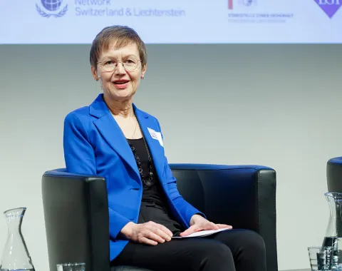 Eine Person in einem blauen Blazer sitzt auf einem Podium und spricht bei einer Veranstaltung an der Universität Liechtenstein. Im Hintergrund sind Logos von Partnerorganisationen zu sehen.