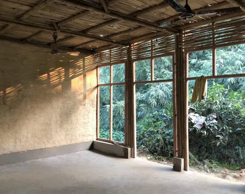 Innenansicht eines Schulgebäudes in Bahuarwa, Indien, mit Wänden aus natürlichen Materialien und großen Fenstern, die viel Tageslicht hereinlassen. Draußen ist üppige Vegetation zu sehen.