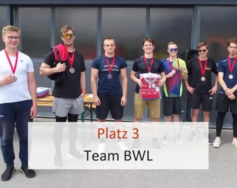 Eine Gruppe von sieben jungen Männern steht nebeneinander und trägt Medaillen um den Hals. Sie halten eine Urkunde und lächeln in die Kamera. Im Vordergrund steht der Text "Platz 3 Team BWL".