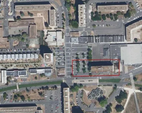 Luftbild einer städtischen Umgebung mit mehreren Gebäuden und Straßen. Ein Bereich ist rot umrandet, möglicherweise zur Hervorhebung eines spezifischen Projekts oder Standorts.