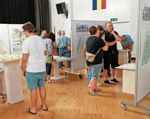 Menschen betrachten Architekturmodelle und Plakate in einer Ausstellungshalle. Die Veranstaltung zeigt studentische Projekte zur Ortsentwicklung in Ruggell, präsentiert von der Universität Liechtenstein.