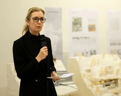 Eine Frau mit blonden Haaren und schwarzer Kleidung hält eine Rede