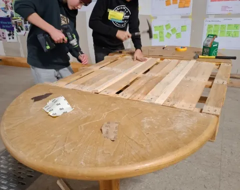 Zwei Jugendliche arbeiten an einem Holztisch