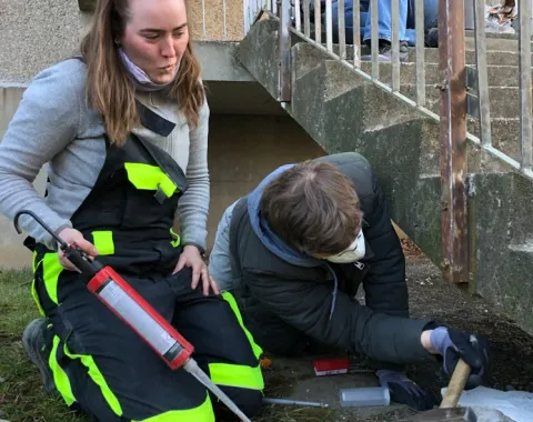 Zwei junge Leute in Arbeiterkleidung arbeiten an einer Aussentreppe