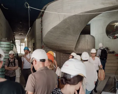 Eine Gruppe von Menschen mit Bauhelmen, die auf einer Baustelle geführt werden. 