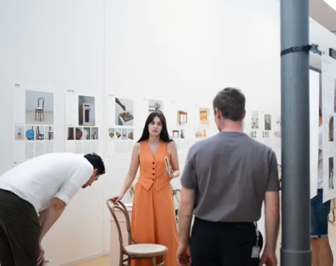 Zwei Männer und eine Frau mit oranger Kleidung stehen in einer Ausstellung 