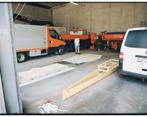 Eine Werkstatt mit Fahrzeugen und einem Holzgerüst für ein Boot. 