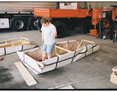 Eine junge Frau steht in einer Werkstatt in einem selbstgebauten Boot. 