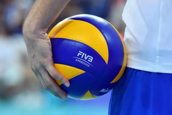 Person, die vor einem unscharfen Hintergrund einen blau-gelben Volleyball mit der Aufschrift „FIVB Approved“ hält.