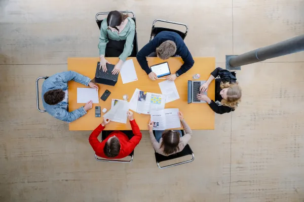 Studierende der Universität Liechtenstein arbeiten an einem Gruppentisch mit Laptops und Unterlagen im modernen Lernbereich.